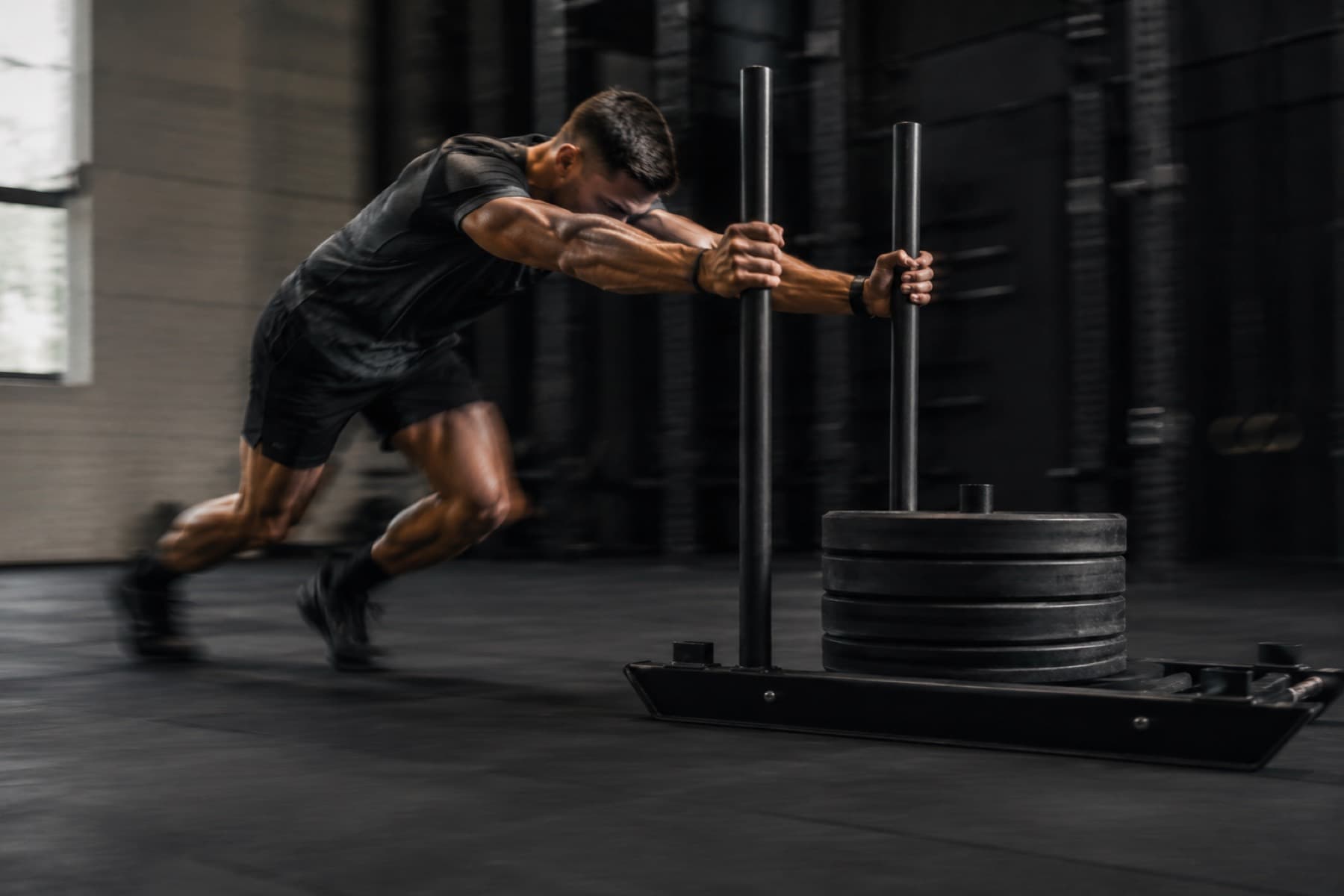 Athlete driving a loaded sled across a dark gym floor